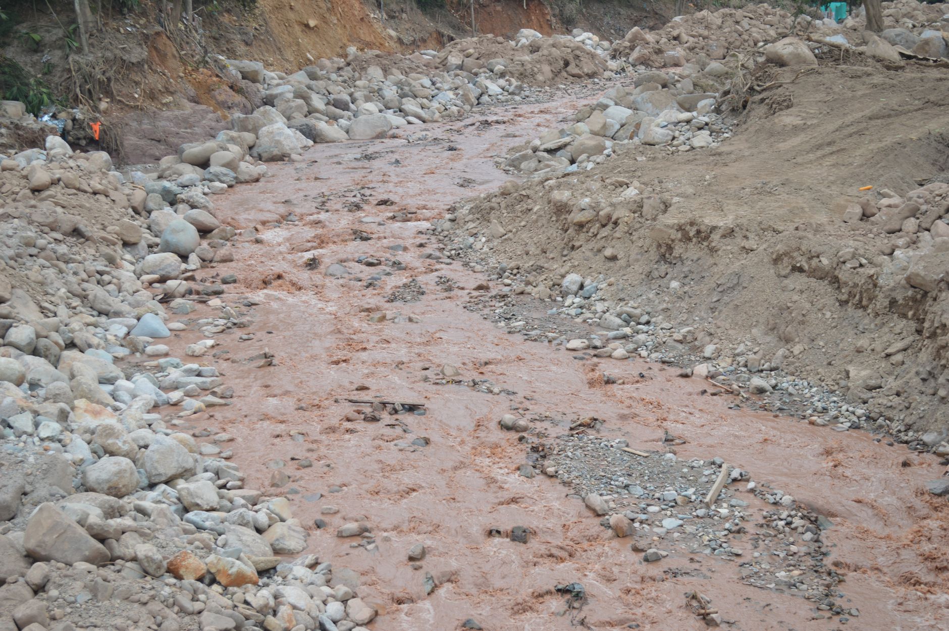 Cours d’eau boueux brun-rouge dans un lit de pierres, entre des berges de terre érodées.